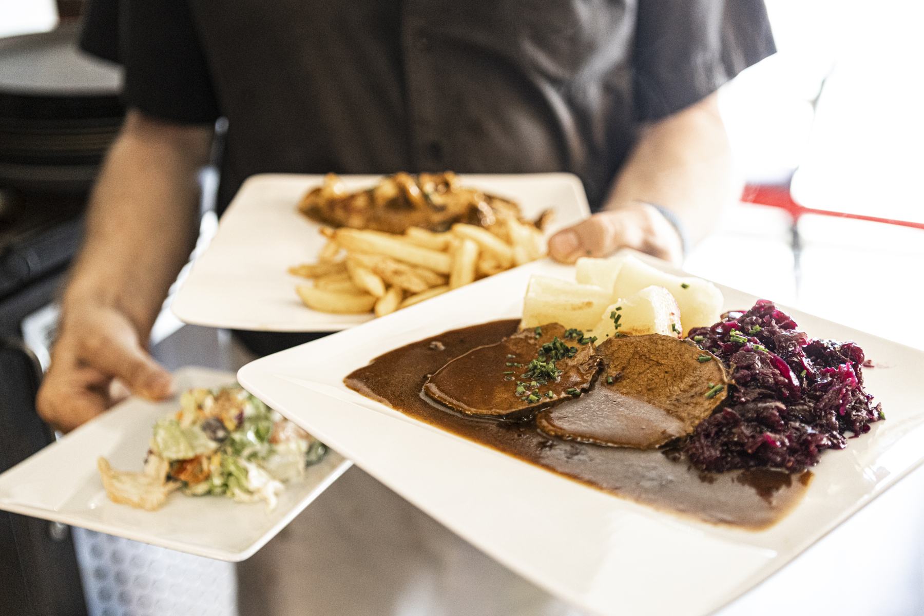 Teller mit Braten, Rotkohl und Pommes werden serviert